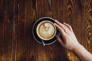 cup of coffee on table with woman's hand touching it