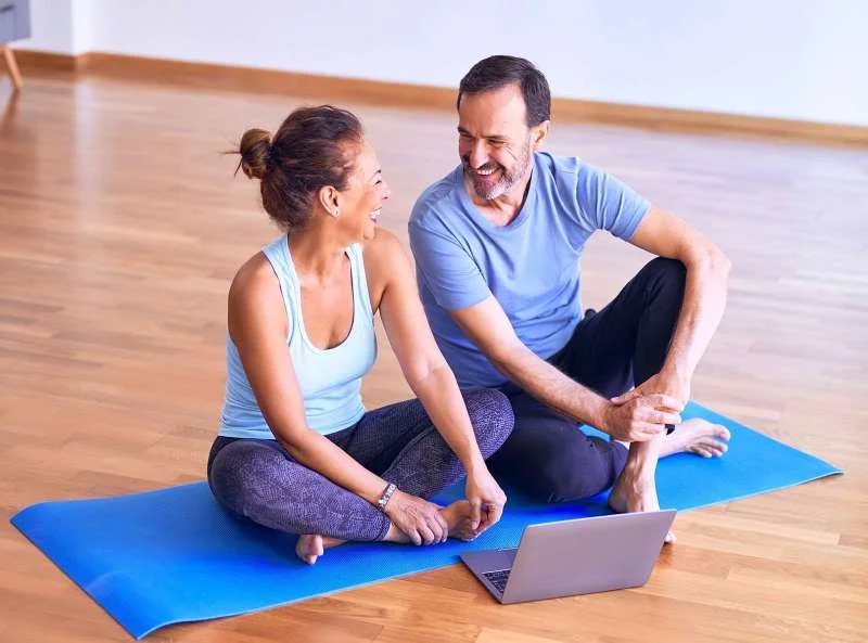 smiling older couple sitting next to each other on an exercise mat